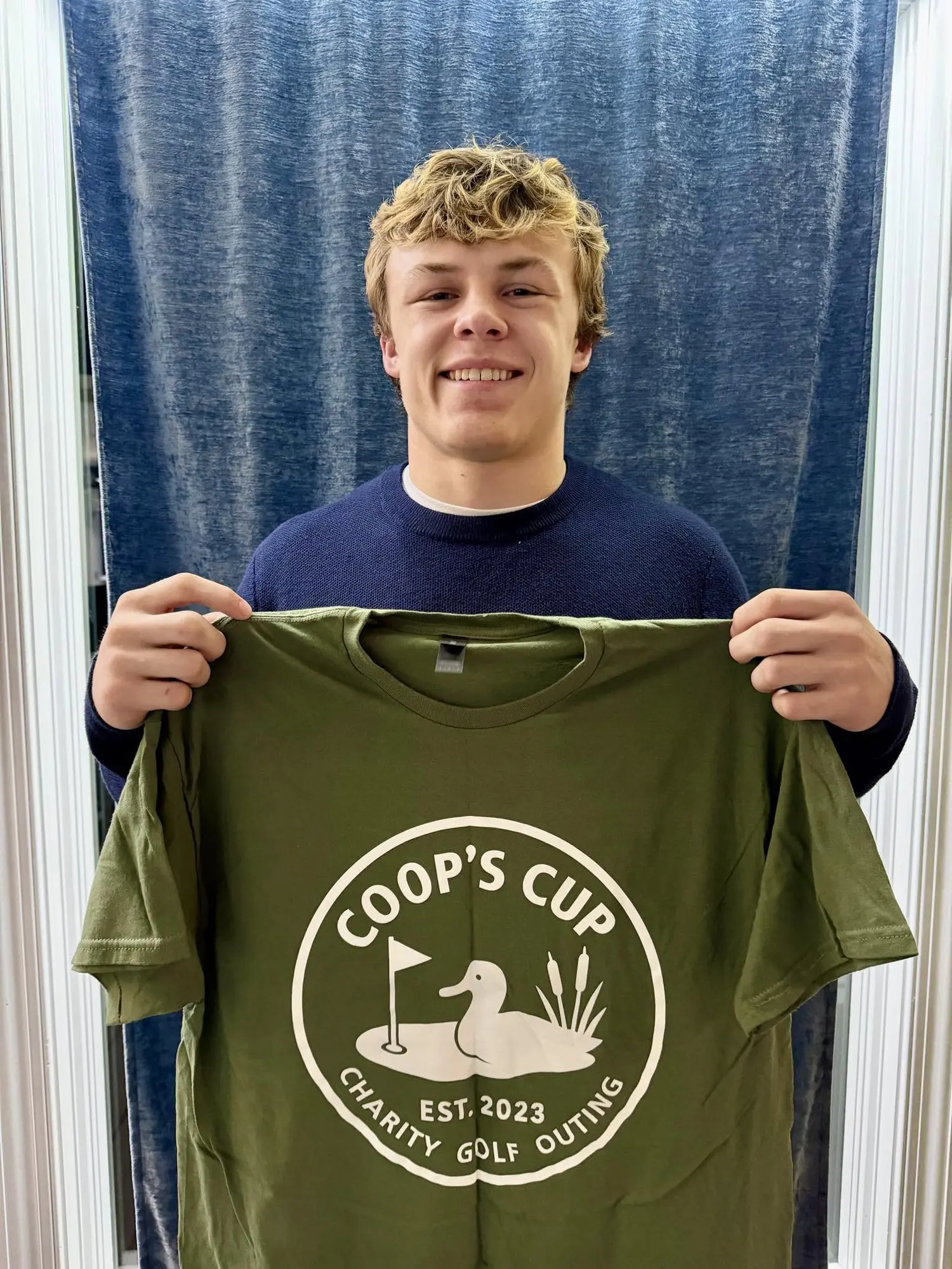 Haakon Peterson holding a green Coop's Cup shirt